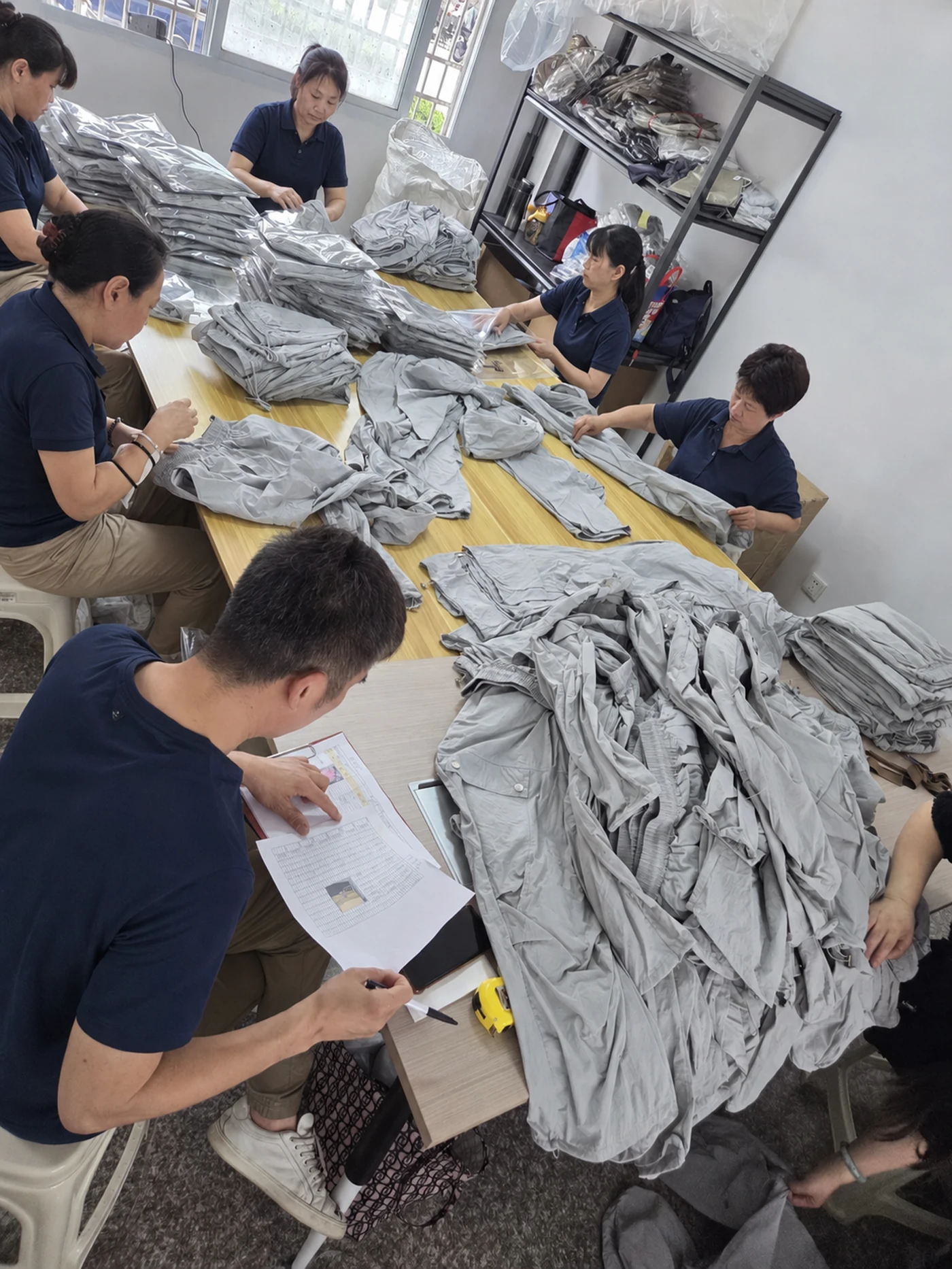 Staff checking a QC sheet and inspecting finished garments on the floor in China